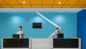Una recepción con dos empleados, una pared azul y un techo blanco y amarillo.