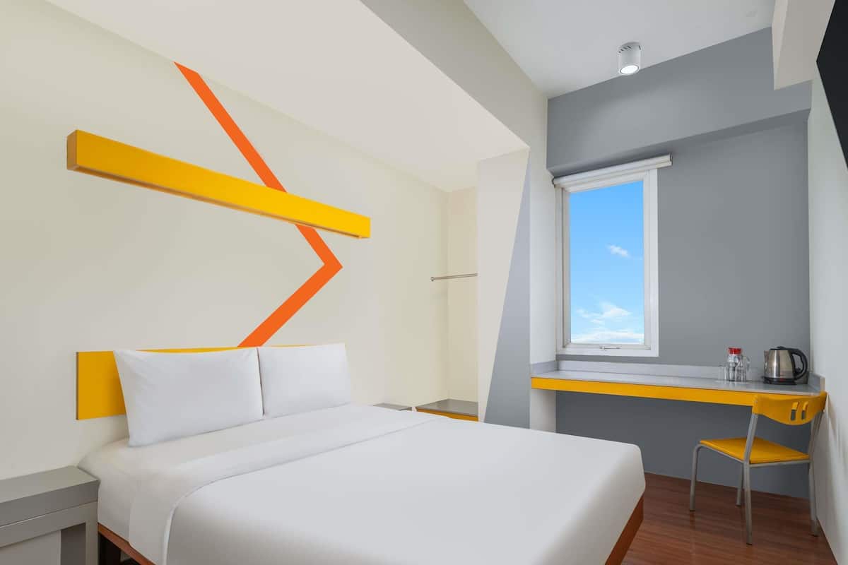 A modern hotel room with a bed, a desk, and a window.