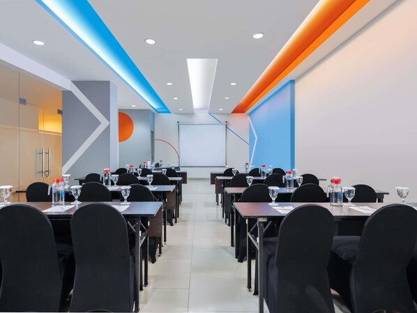 Un salón de conferencias con mesas, sillas, una pantalla de proyector y una pizarra.