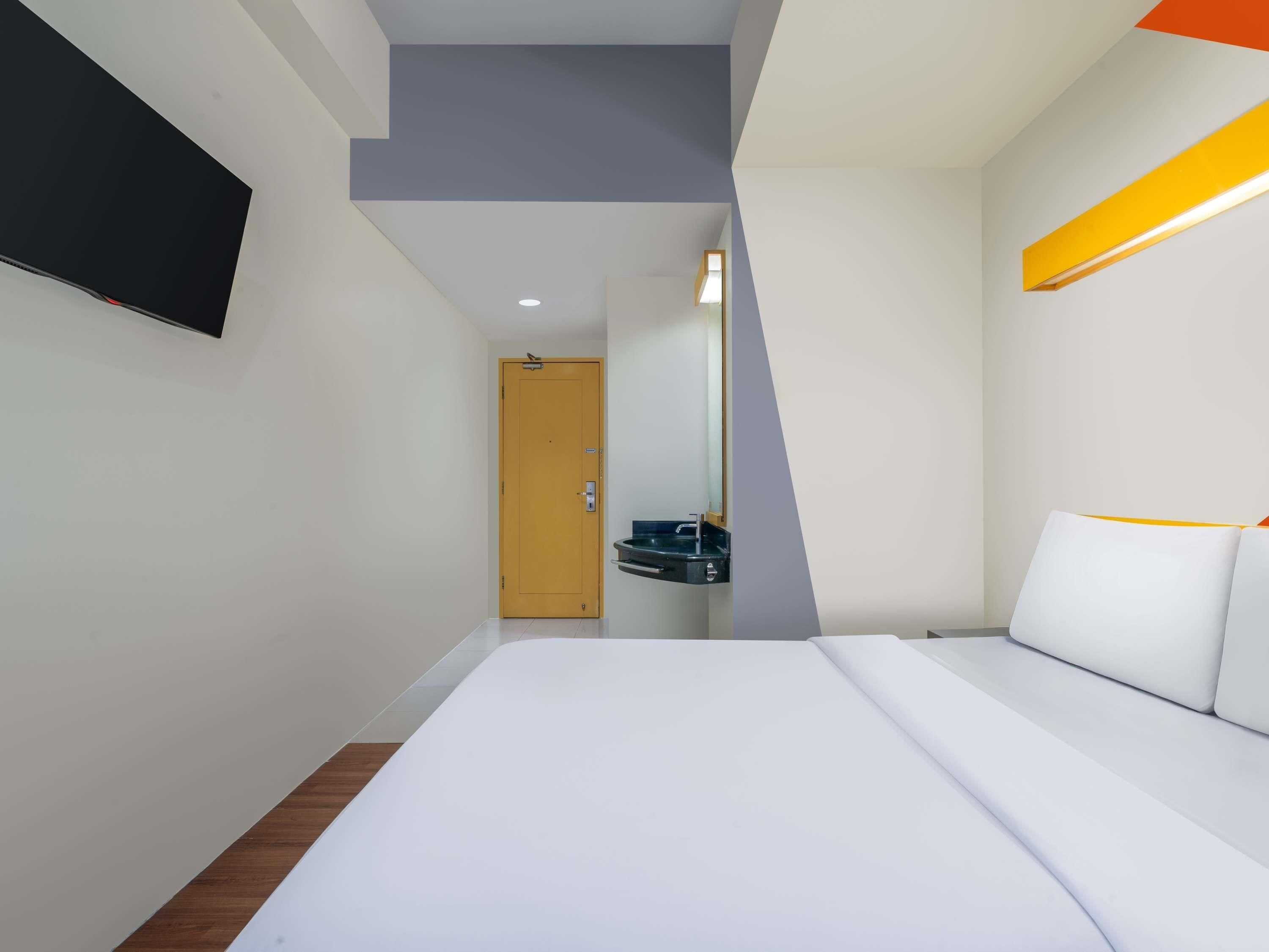 A modern hotel room with a bed, a bedside table, a mirror, and a television mounted on the wall.