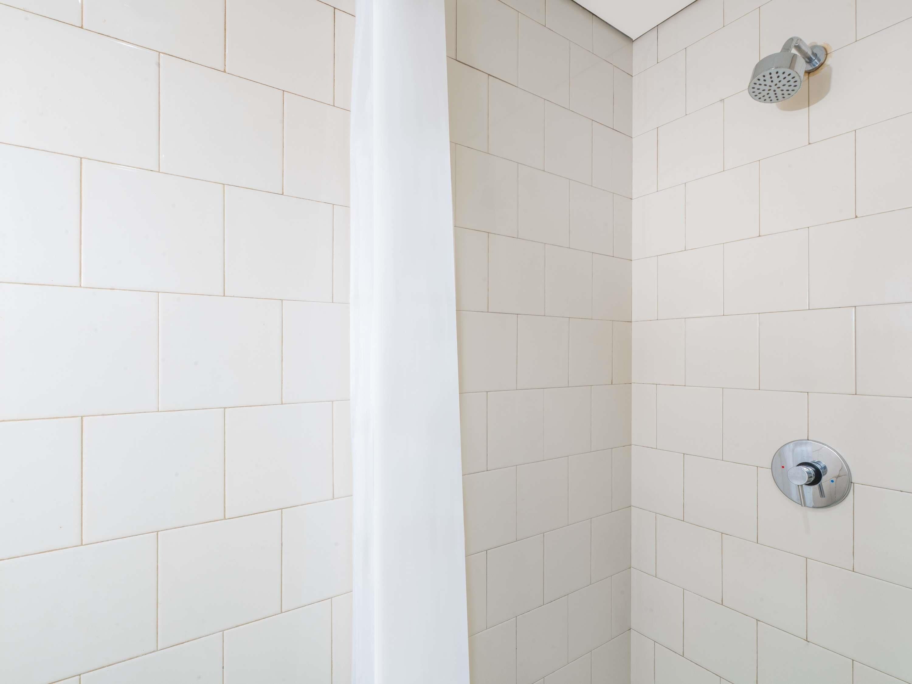A shower area with white tiles, a showerhead, and a control knob.