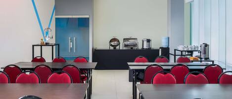 Un comedor moderno con sillas y mesas rojas, una encimera de cocina con electrodomésticos y una pared azul decorativa.