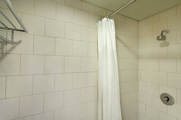 Un área de ducha con azulejos blancos, un cabezal de ducha y una cortina.