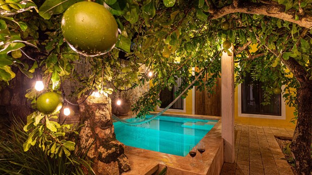 A swimming pool surrounded by lush greenery and stone structures. - Hotel Casa Hipil (Valladolid)