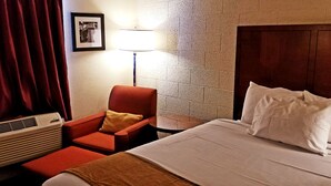 A hotel room with a bed, a red armchair, a lamp, and a picture on the wall.