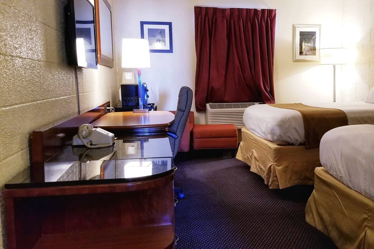 A hotel room with two beds, a desk with a telephone, a chair, a wall-mounted TV, and a picture frame.