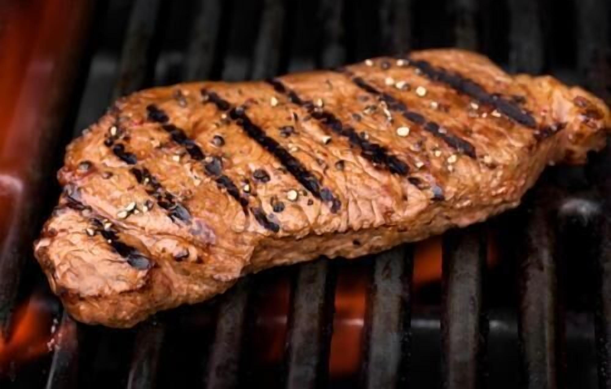 Een gegrild steak met duidelijke grillstrepen en kruiden op een barbecue.