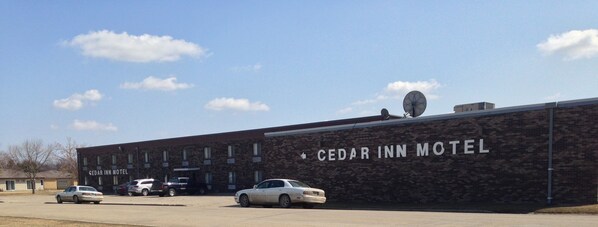 The exterior of Cedar Inn Motel with a brick facade, a satellite dish, and several parked cars.