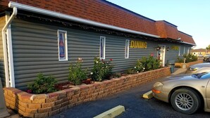 A building with a grey exterior, a 'DINING' sign, and a 'LOUNGE' sign. There is a brick planter with plants and a parked car.