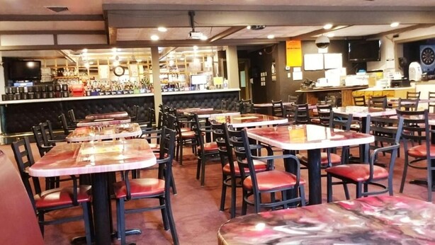 A restaurant interior with multiple tables and chairs, a bar area, and a dartboard.