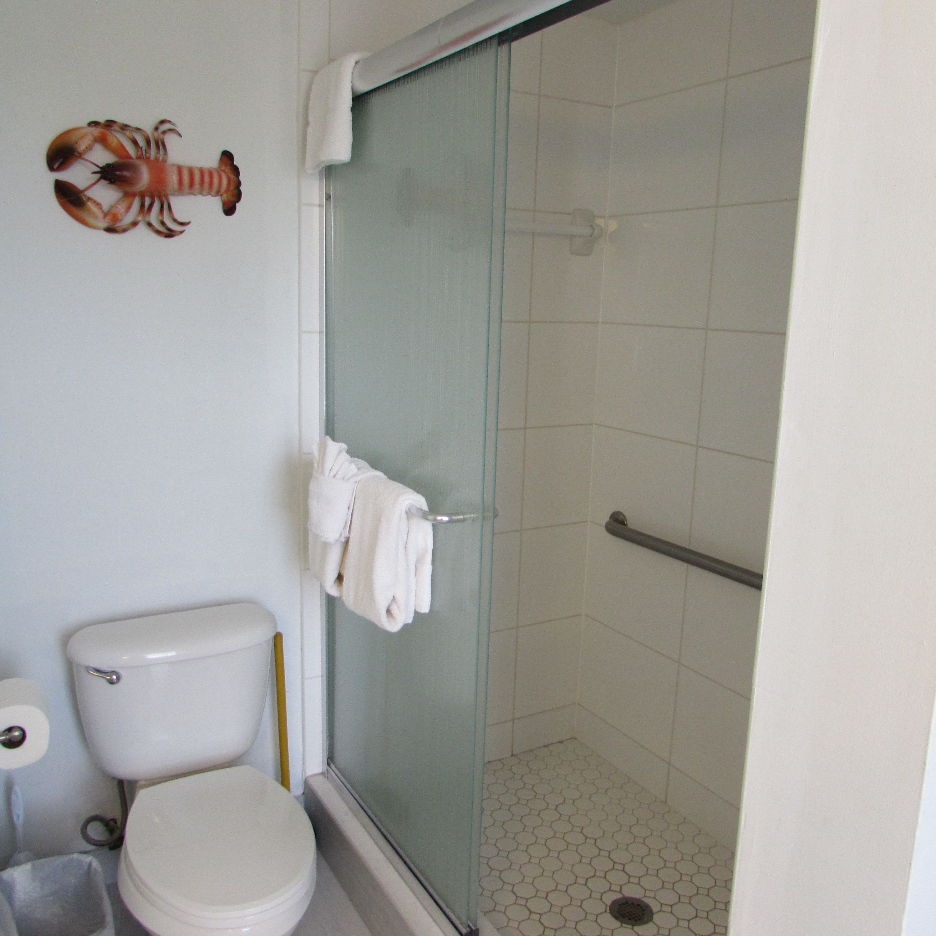 Een badkamer met toilet, een douchecabine van glas en een kreeftdecoratie aan de muur.