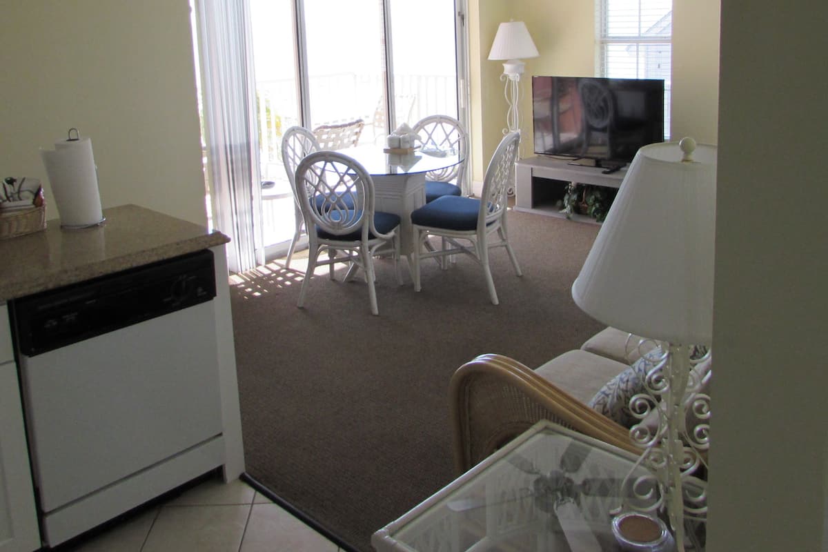 A living room with a ceiling fan, a dining table with chairs, a sofa, a television, and a lamp.