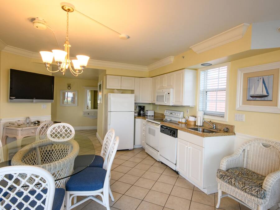 A kitchen with white cabinets, a refrigerator, a microwave, a stove, and a dishwasher. There is a dining table with chairs and a chandelier.