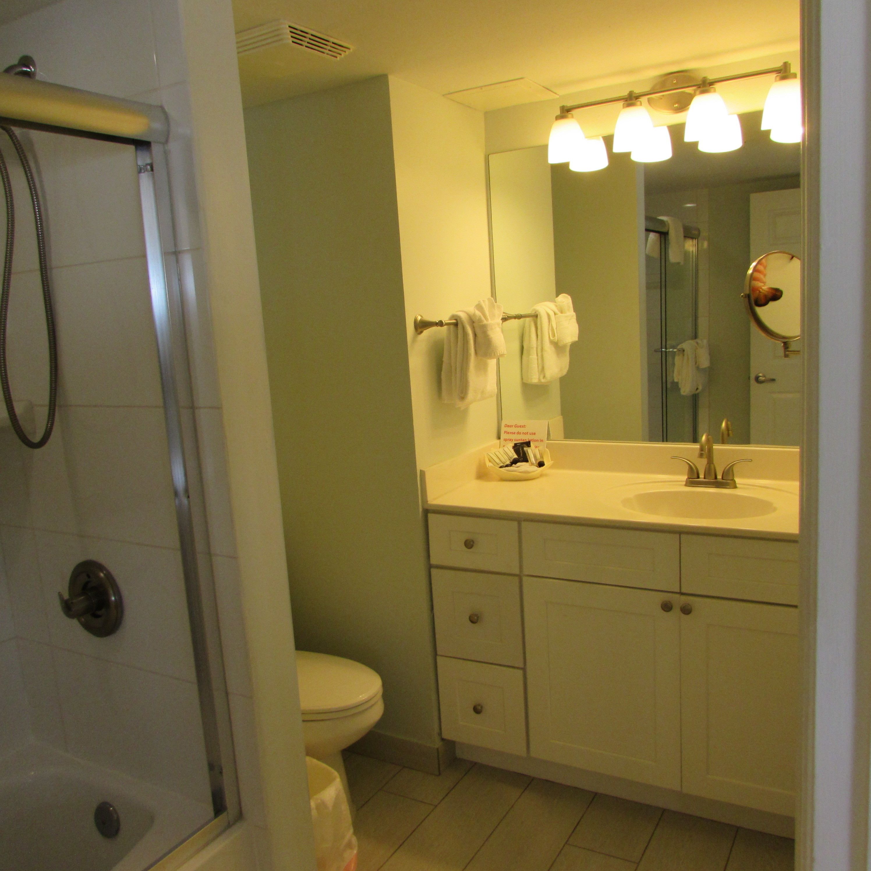 A bathroom with a shower, toilet, sink, and mirror.