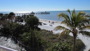 A beach with a pier extending into the water, palm trees, and a clear sky. - Edison Beach House (Fort Myers Beach)