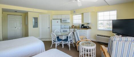 Une chambre de taille modeste comprenant deux lits, un coin cuisine, un espace repas et un téléviseur.