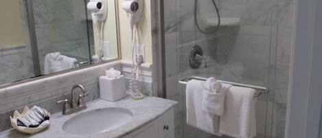 A bathroom with a marble sink, a mirror, a hairdryer, a towel rack, and a glass shower enclosure.