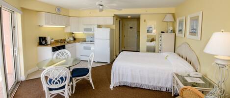 Una habitación de hotel compacta con kitchenette, una cama, zona de comedor y baño.