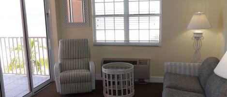 A living room with a ceiling fan, a striped armchair, a round table, a sofa, and a window with blinds.
