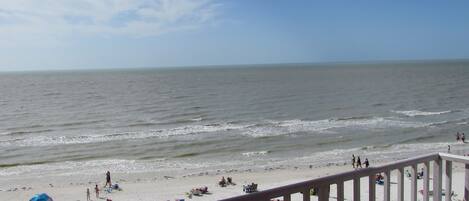 A beach with people and umbrellas, a railing, and the ocean.