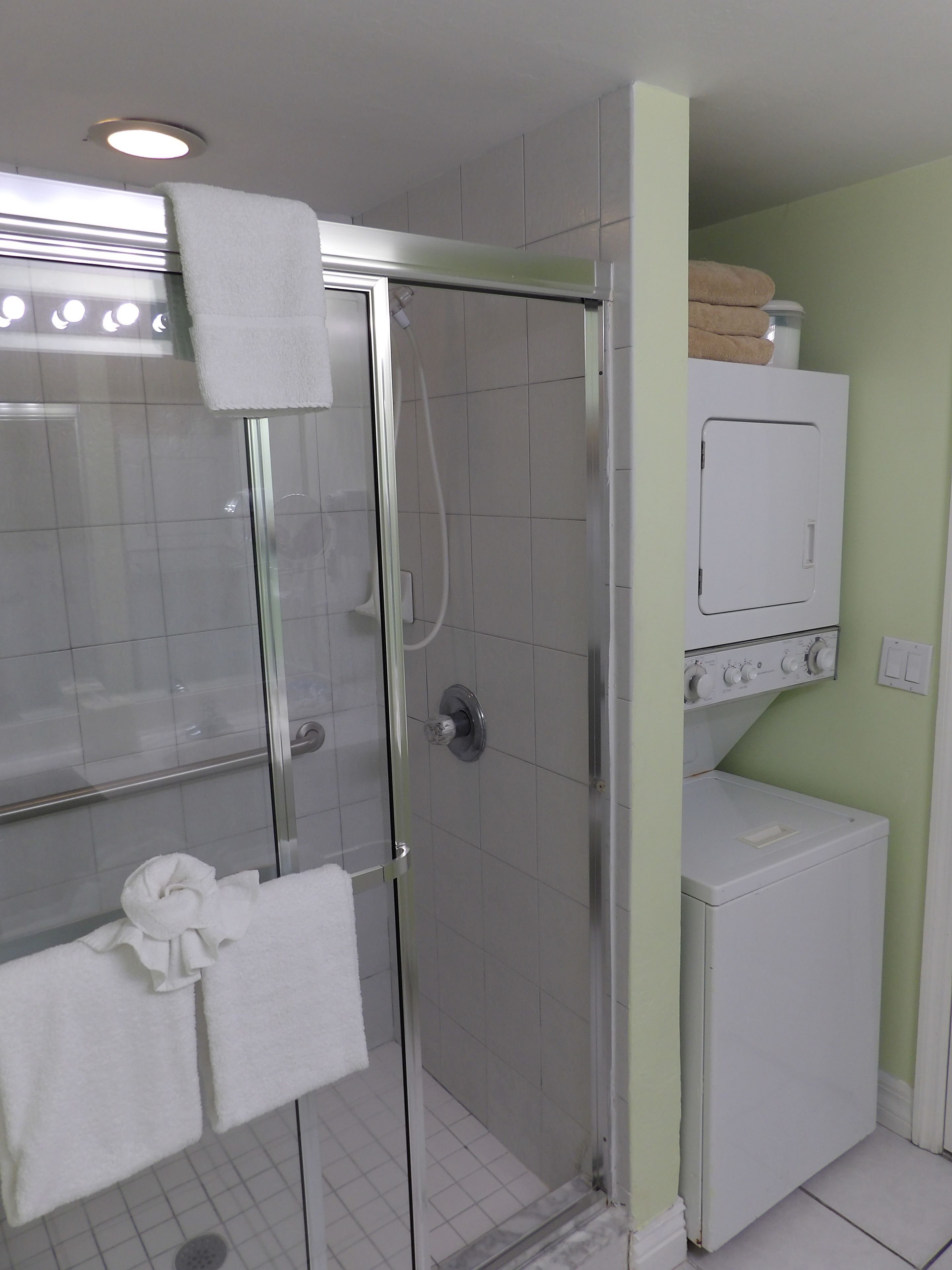 A bathroom with a glass-enclosed shower, a white washing machine, and a towel rack with towels.
