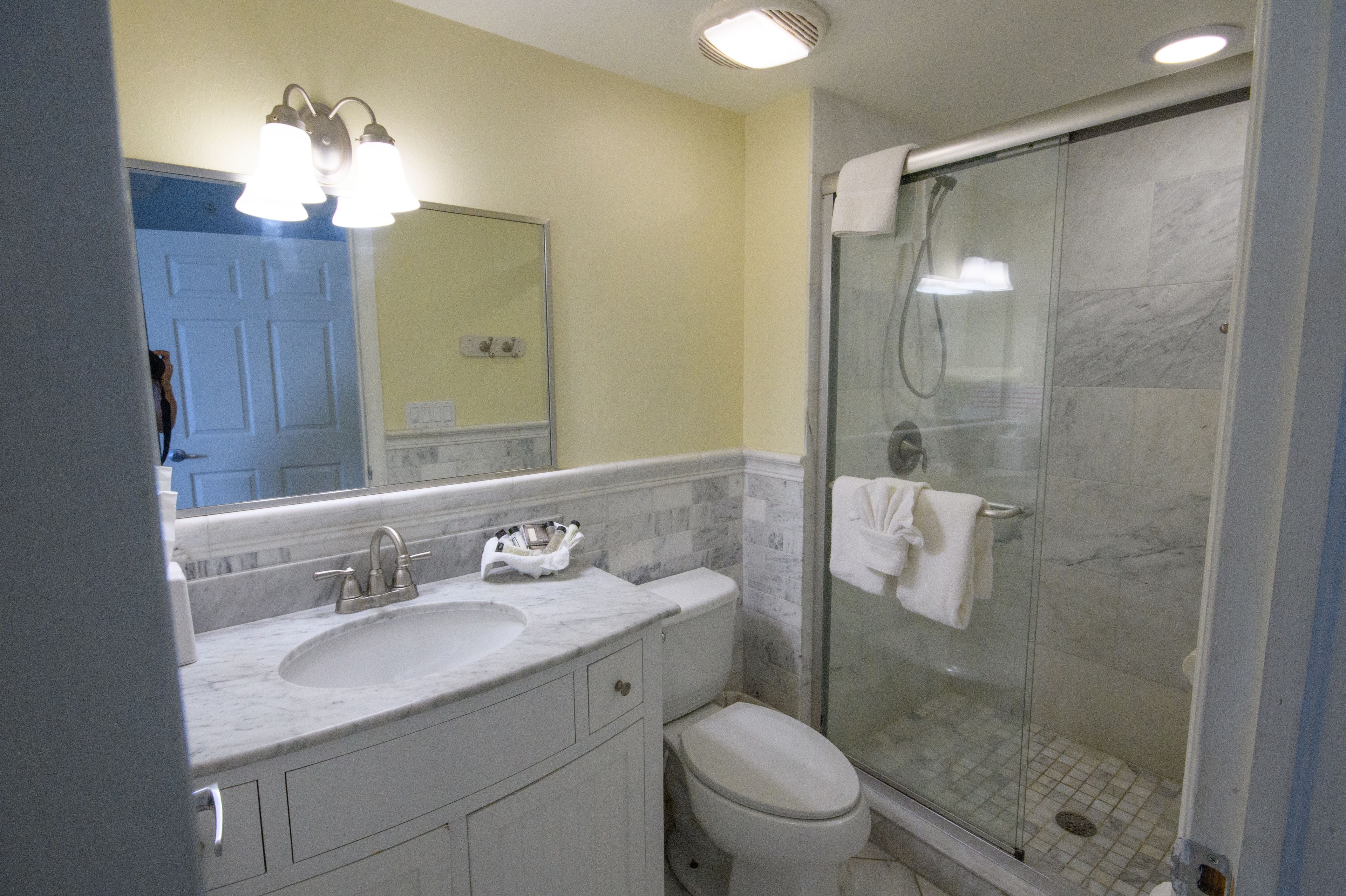 A bathroom with a marble sink, a toilet, a glass shower enclosure, and a mirror with lights.