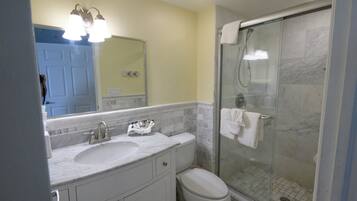 A bathroom with a marble sink, a toilet, a glass shower enclosure, and a mirror with lights.