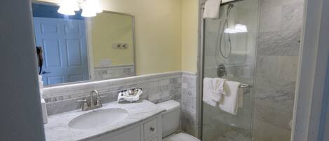A bathroom with a marble sink, a toilet, a glass shower enclosure, and a mirror with lights.