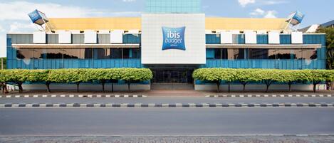 Un bâtiment moderne, facilement reconnaissable grâce à son panneau « ibis budget » bien visible, qui se distingue par son design épuré et contemporain, son aménagement paysager symétrique et son entrée dallée.