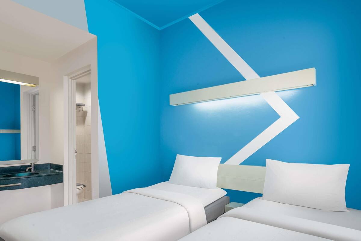 Habitación de hotel con dos camas, un baño con pared de acento azul y un diseño moderno.