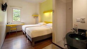 Quarto de hotel com duas camas, uma escrivaninha, uma cadeira, uma janela e banheiro com pia e espelho.