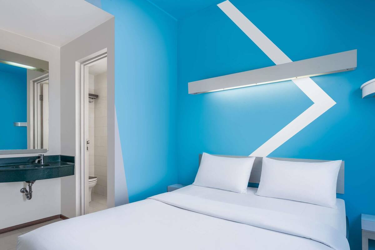 Habitación de hotel moderna con cama, baño con lavamanos y pared decorada en azul.