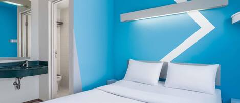 Habitación de hotel moderna con cama, baño con lavamanos y pared decorada en azul.