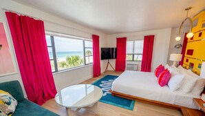 Ein Hotelzimmer mit Bett, Fernseher, Fenster mit Blick auf den Strand und einem kleinen Tisch.