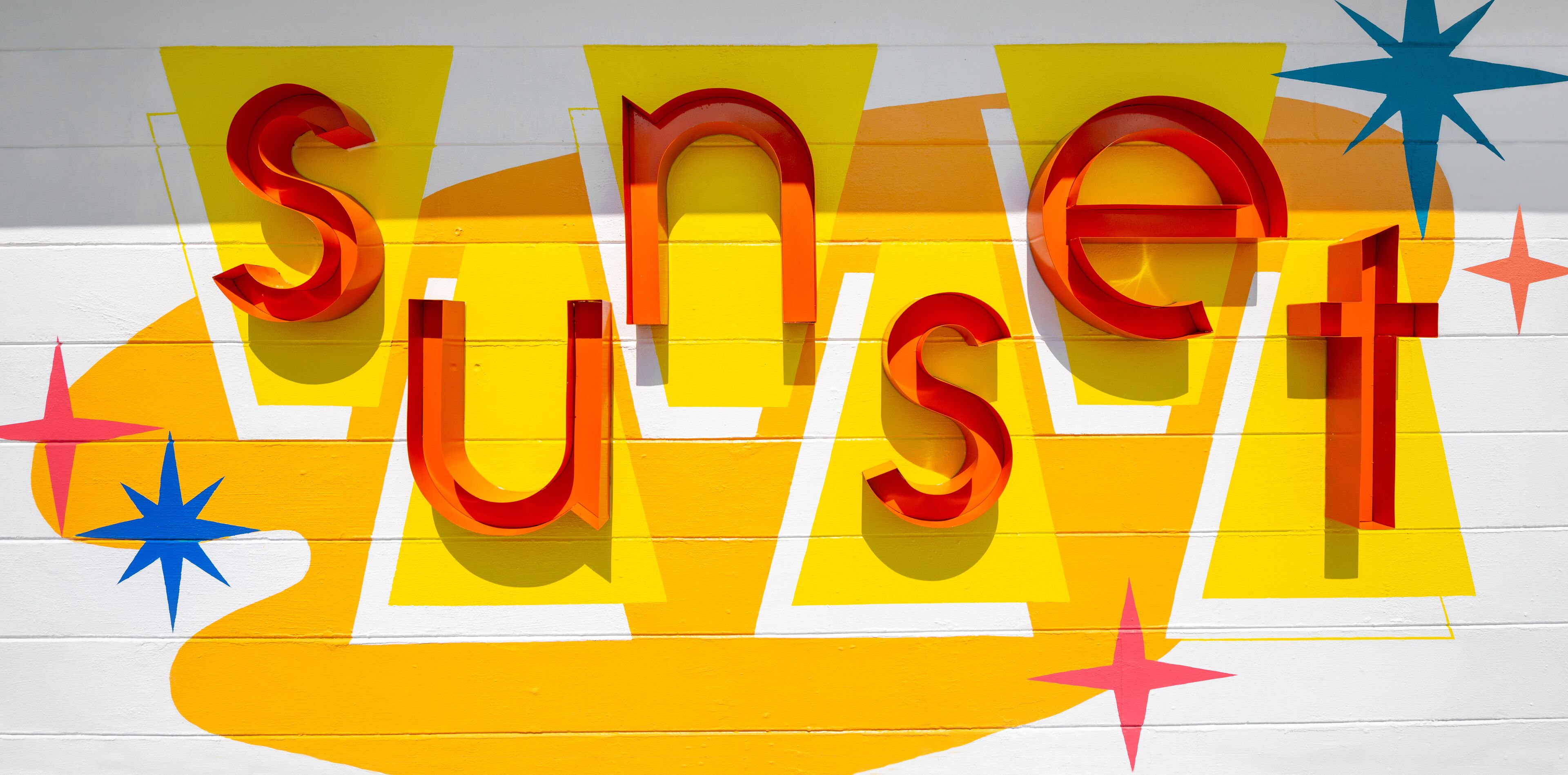 Una pared con letras grandes y coloridas que deletrean “SUNSET” y estrellas decorativas.