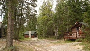 A rustic cabin with a stone chimney, surrounded by dense forest. - Addison's Bungalows (Brisco)