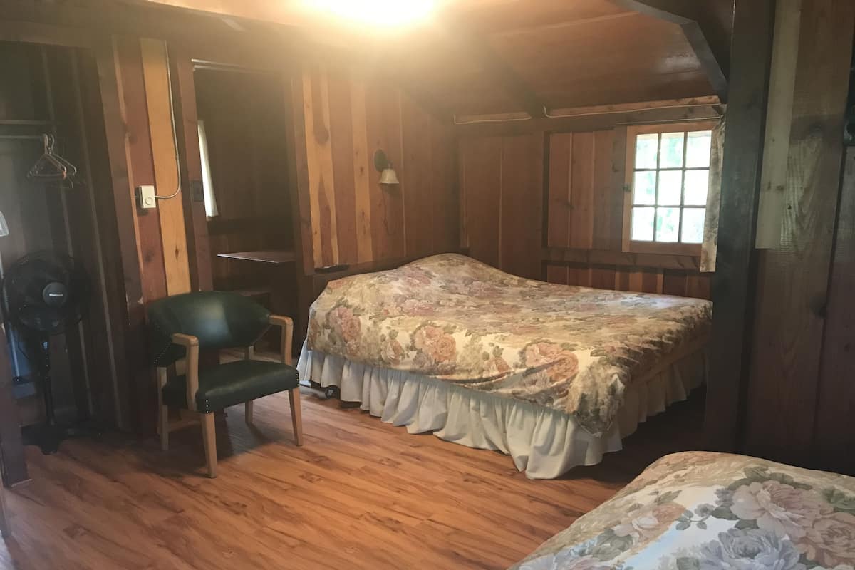 A wooden room with a bed, a chair, and a window.