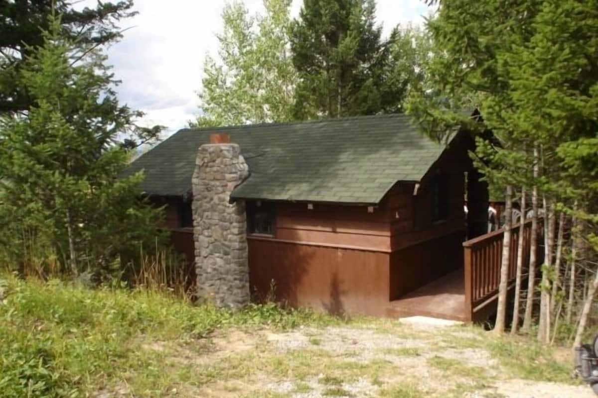 A rustic cabin with a stone chimney, wooden exterior, and a wooden deck.