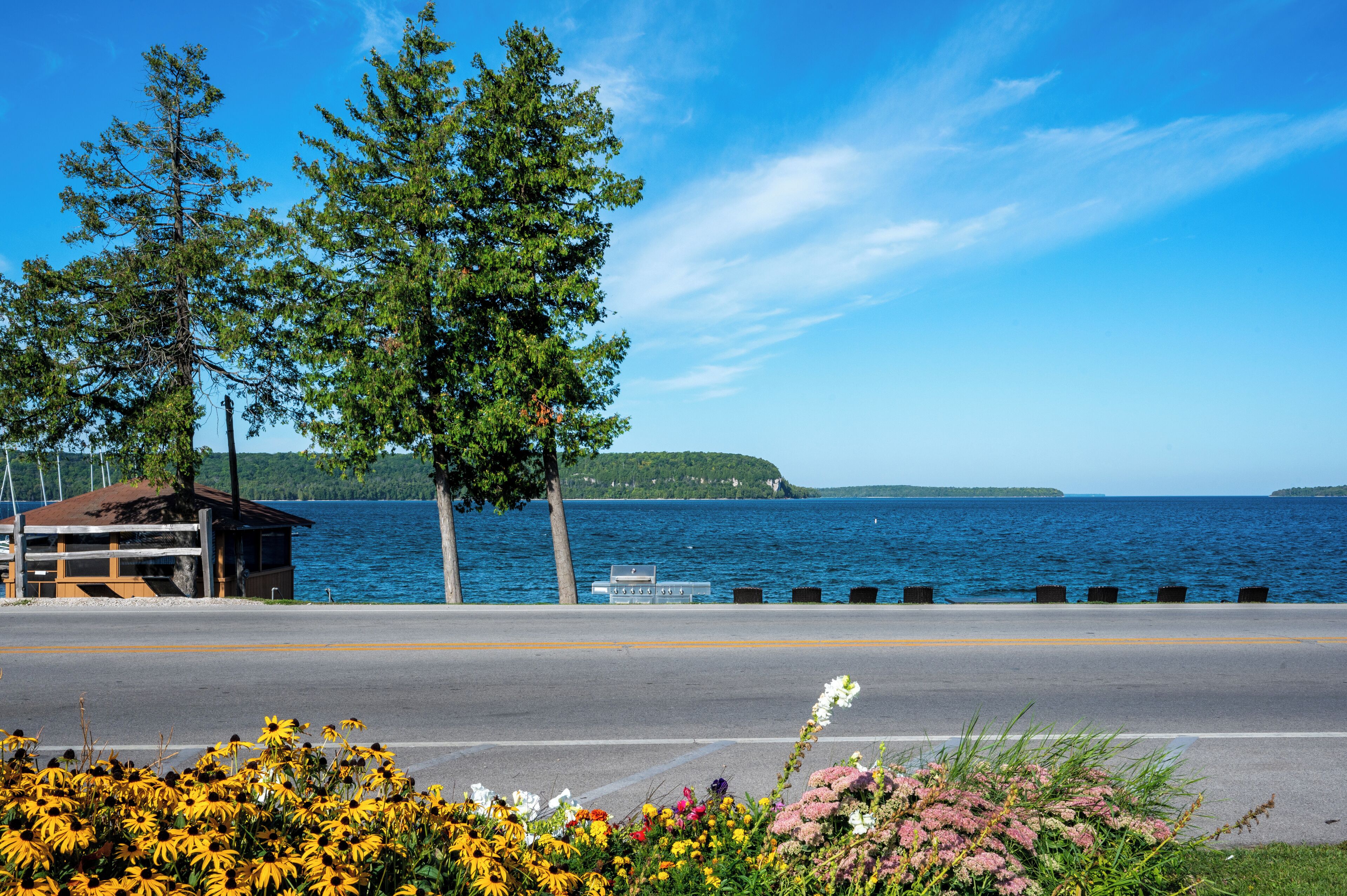 A roadside view with a wooden cabin, a road, and a body of water in the background.