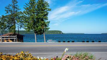 A roadside view with a wooden cabin, a road, and a body of water in the background.