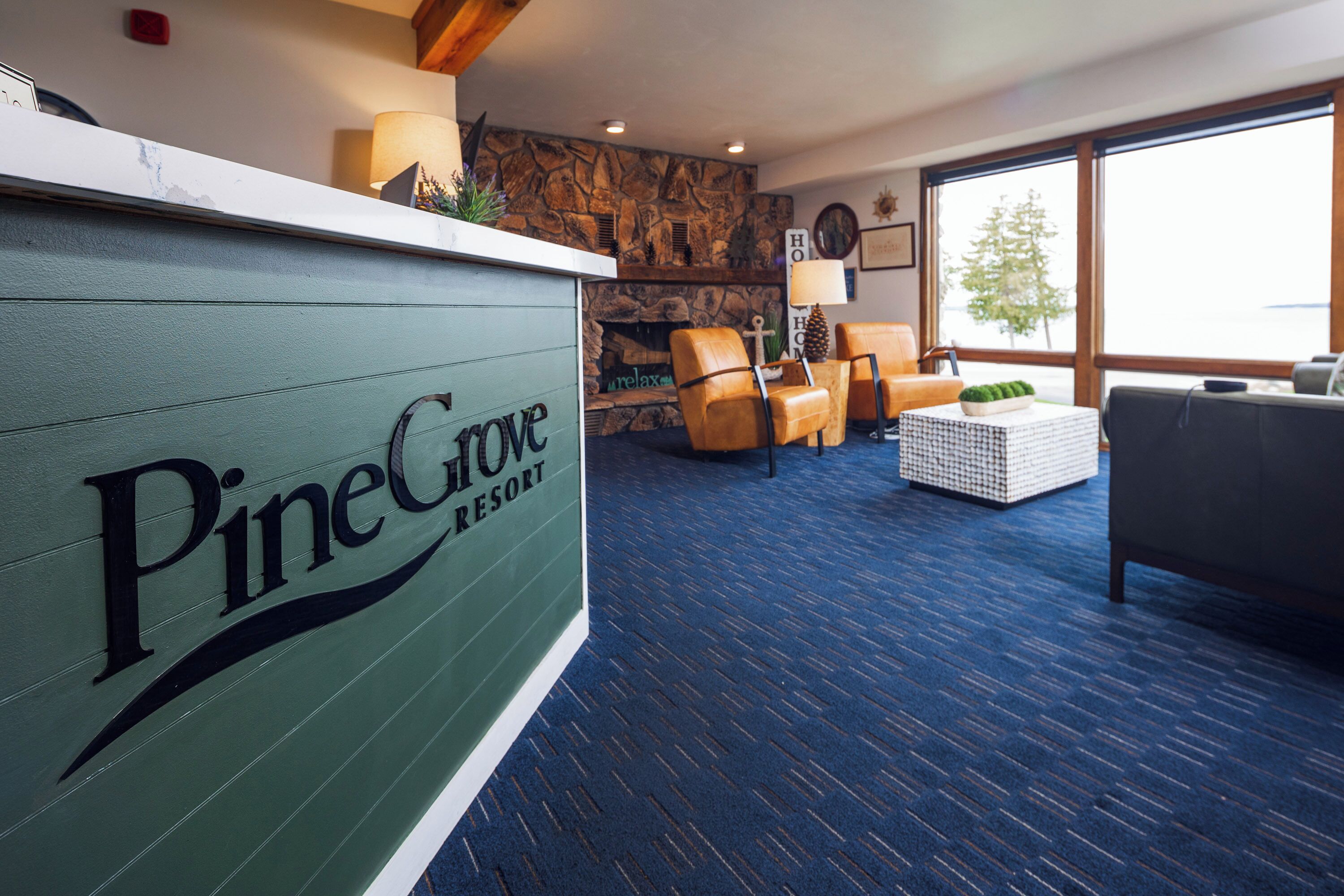Receptionen på Pine Grove Resort har en stenmur, en öppen spis, läderfåtöljer, en soffa och ett stort fönster.