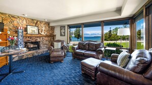 A spacious living room with a stone wall, leather furniture, a fireplace, and a view of the ocean. - Pine Grove Resort (Ephraim)