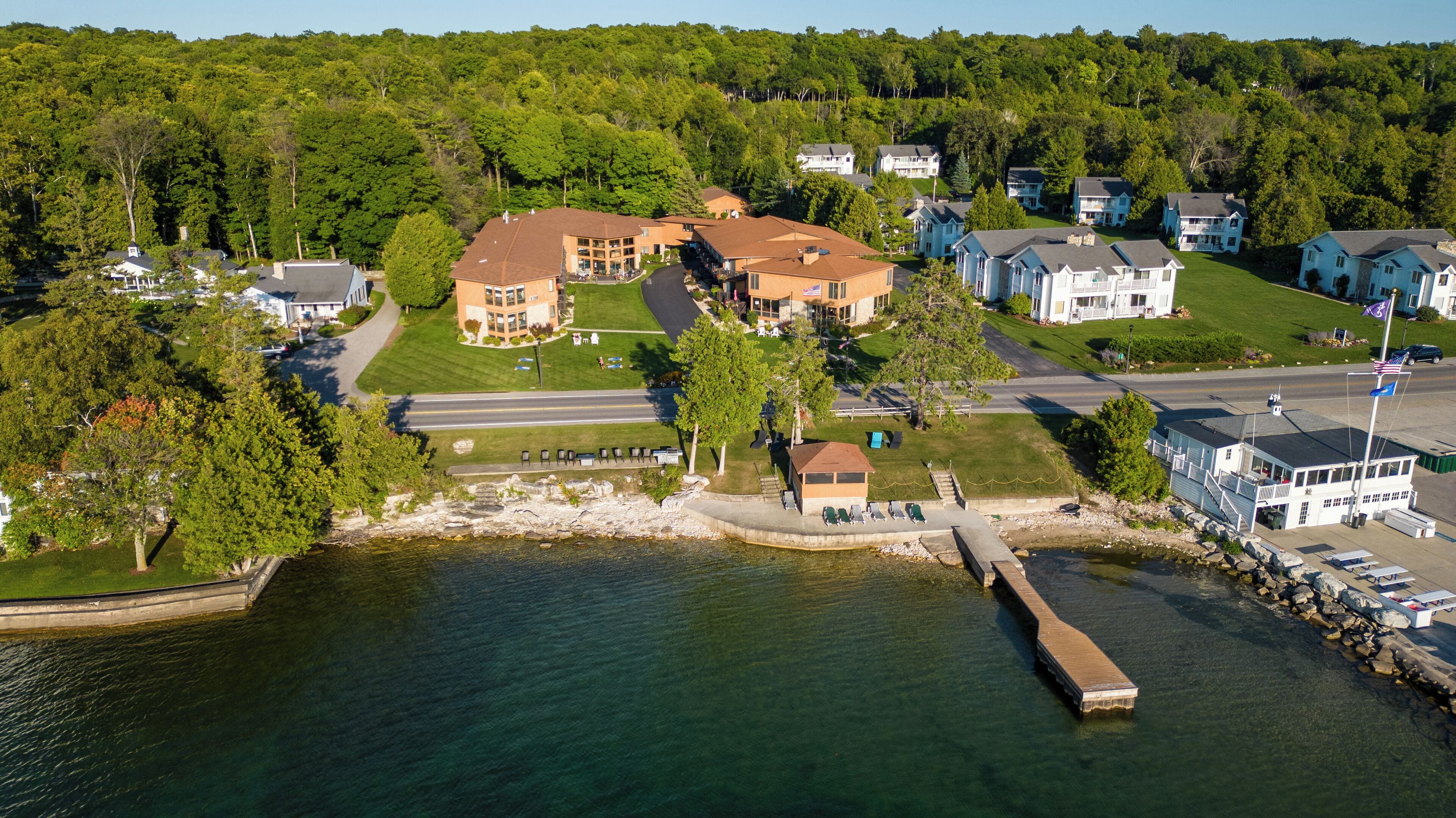An aerial view of a lakeside community with a prominent building featuring a large porch and a dock extending into the water.