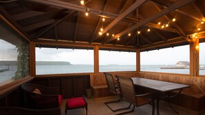 A covered outdoor seating area with a wooden table and chairs, overlooking a body of water. - Pine Grove Resort (Ephraim)