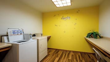 Un cuarto de lavandería con lavadora, secadora y una estantería con una planta.