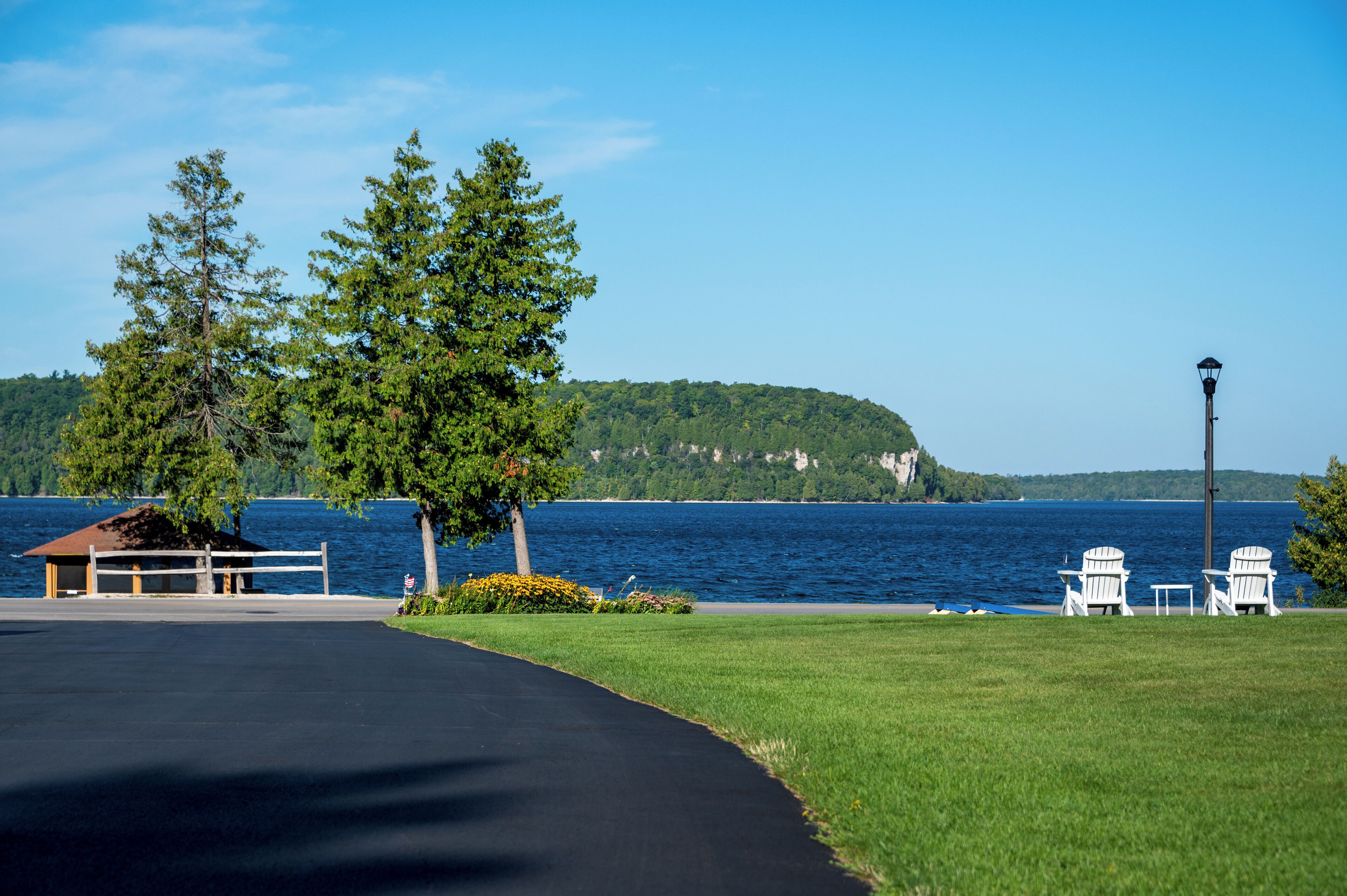 A lakeside view with a gazebo, two Adirondack chairs, and a lamp post.