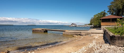 A beach with a wooden pier extending into calm waters, a small dock, and a building with a red roof near the shore.