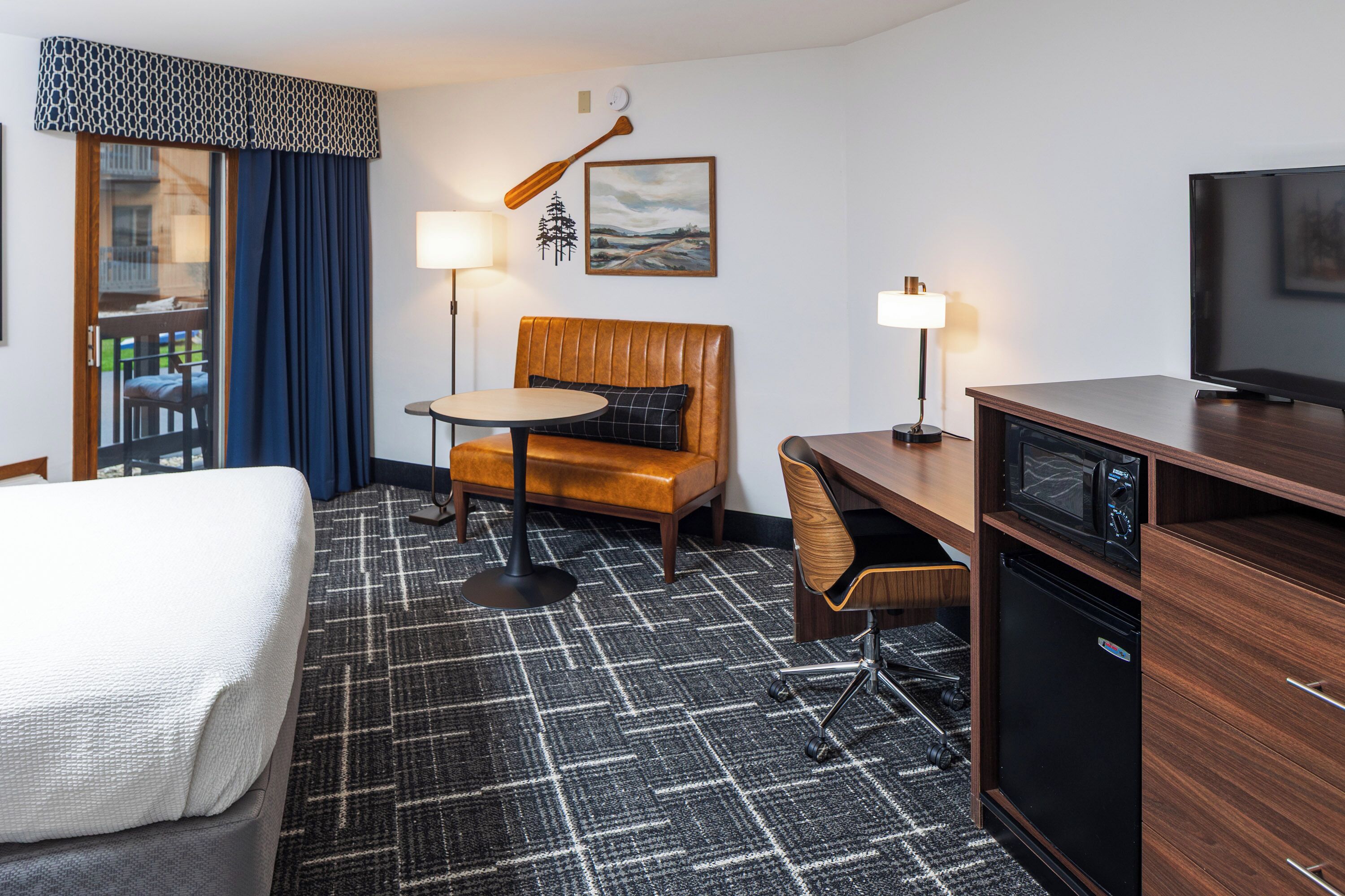 A hotel room with a bed, a desk, a chair, a television, a microwave, and a small refrigerator.
