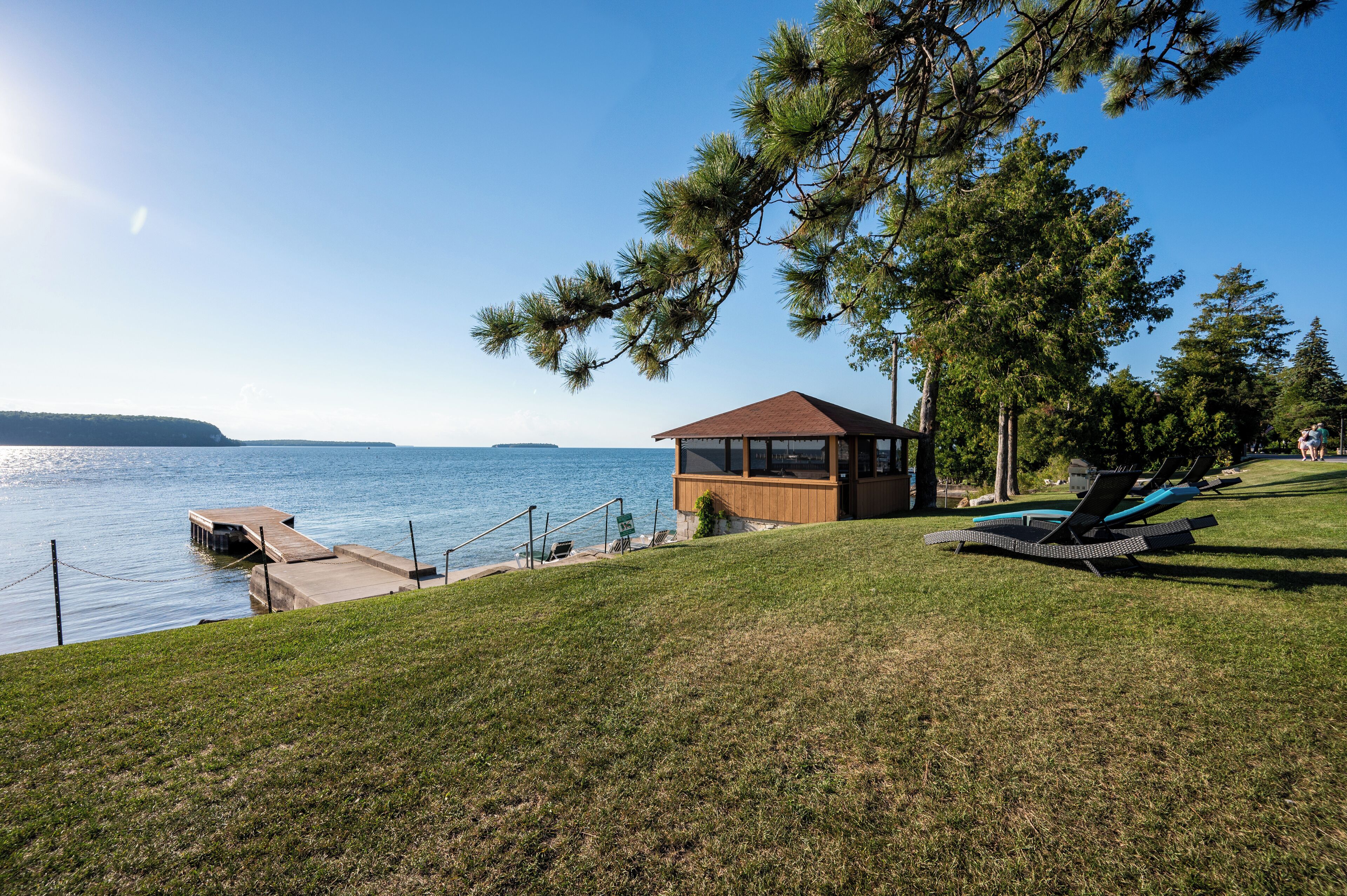 Un chalet au bord du lac, avec une cabane en bois, un quai et des chaises longues disposées sur une pelouse.