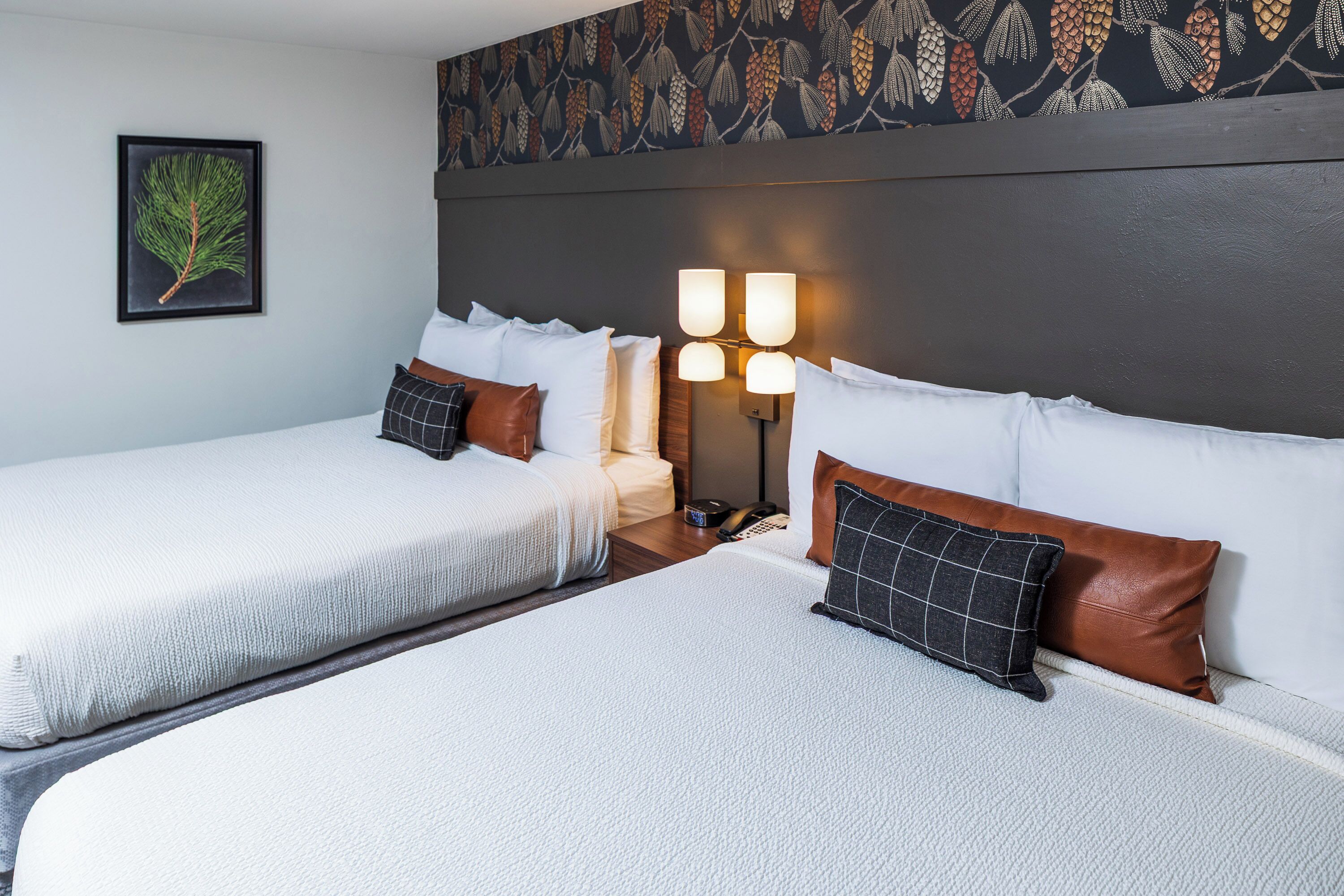 A hotel room with two beds, a nightstand, a lamp, and a wall with a leaf pattern.